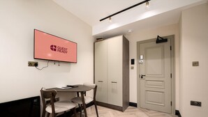 A modern hotel room with a dining area, a flat-screen TV, a wardrobe, and a door. - Guestready - The Euston Hotel (London)
