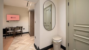 A hotel hallway with a wooden floor, a round mirror, a trash bin, and a television displaying "GUEST READY". - Guestready - The Euston Hotel (London)