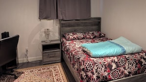 Une chambre à coucher avec un lit, un bureau, une lampe et une fenêtre avec des rideaux.