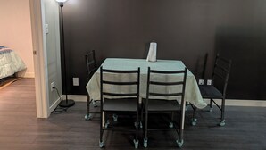 Un coin repas avec une table dressée pour quatre personnes, des chaises, une lampe et un lit en arrière-plan.