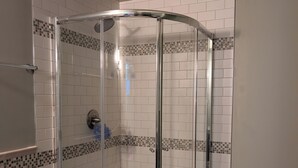 Une douche fermée par des parois de verre, avec des carreaux blancs et une petite fenêtre.