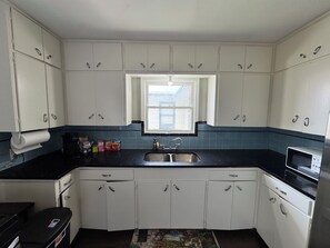 A compact kitchen with white cabinets, a black countertop, a window, and a microwave. - Charming 2BR in Monticello Park
Covered parking, Near Downtown/ Pearl (San Antonio)