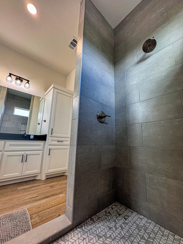 A modern bathroom with a shower, tiled walls, and a wooden floor. - Out of Bounds Pool Frio River Sleeps 24 (Concan)