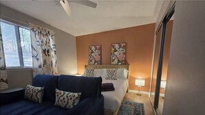 Una habitación de hotel con una cama, un sofá azul, un ventanal con cortinas y dos obras de arte en la pared.