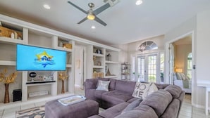 A living room with a sectional sofa, a flat-screen TV, and a ceiling fan.