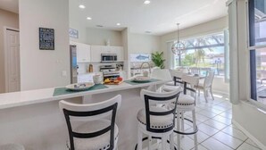 A modern kitchen with white cabinets, a dining area with white chairs, and a view of the outdoors through large windows.
