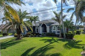 A residential house with a front lawn, palm trees, and a clear sky. - Casa Blanca (Cape Coral)