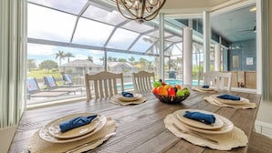 A dining area with a large table, chairs, and a view of a pool and palm trees.