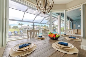 A dining area with a view of a pool and palm trees, a chandelier, and a table set with plates and napkins. - Casa Blanca (Cape Coral)