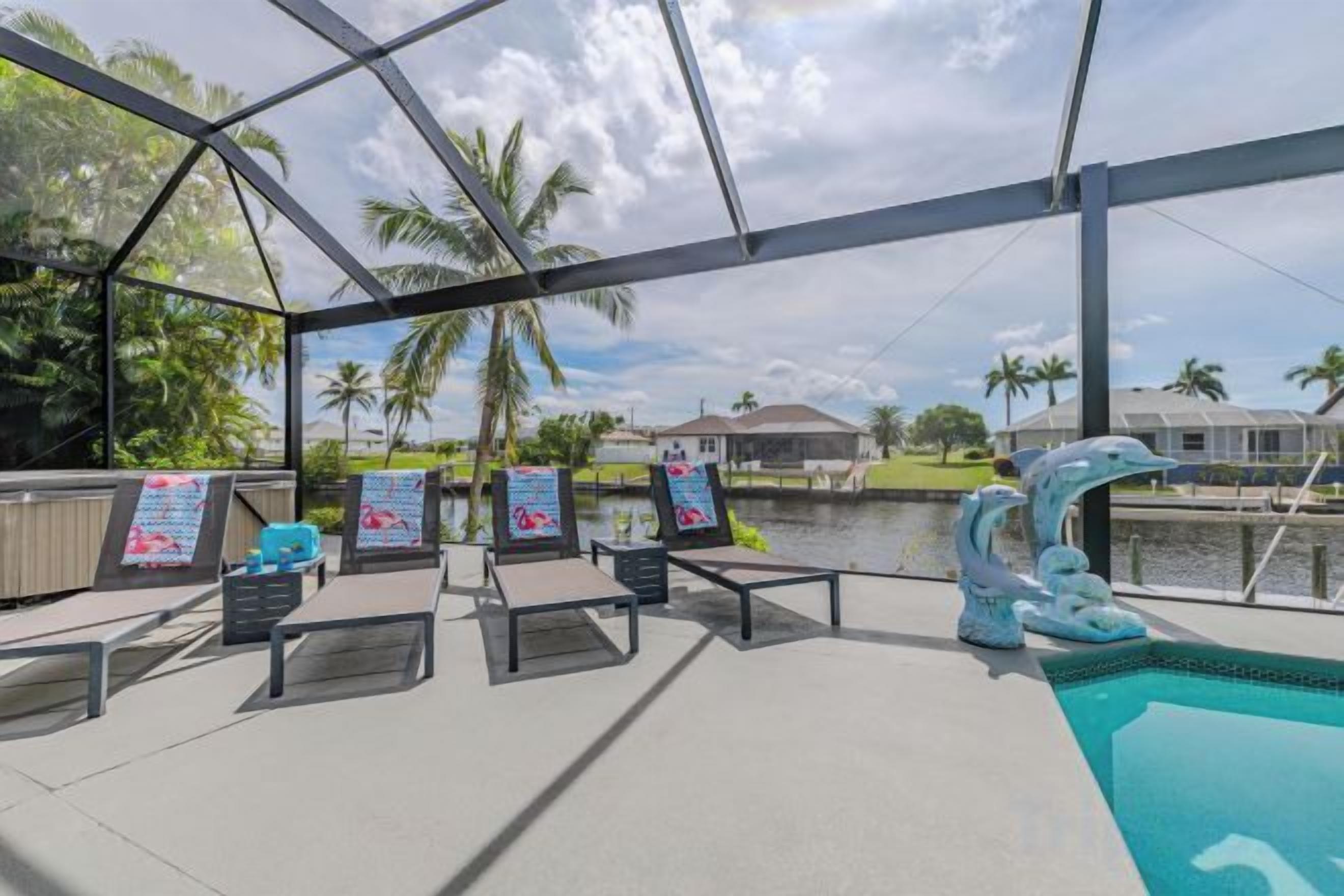 A poolside area with lounge chairs, a pool, and a view of a body of water and palm trees.