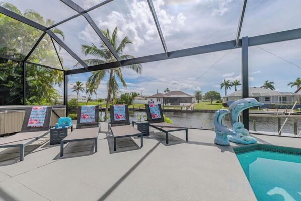 A poolside area with lounge chairs, a pool, and a view of a body of water and palm trees. - Casa Blanca (Cape Coral)
