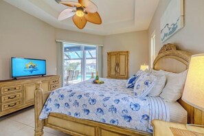 A bedroom with a bed, a television, a ceiling fan, and a view of the outside. - Casa Blanca (Cape Coral)