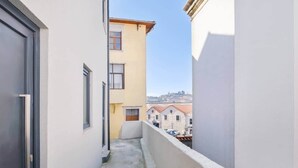 Een smal balkon met uitzicht op omliggende gebouwen en een verafgelegen landschap.