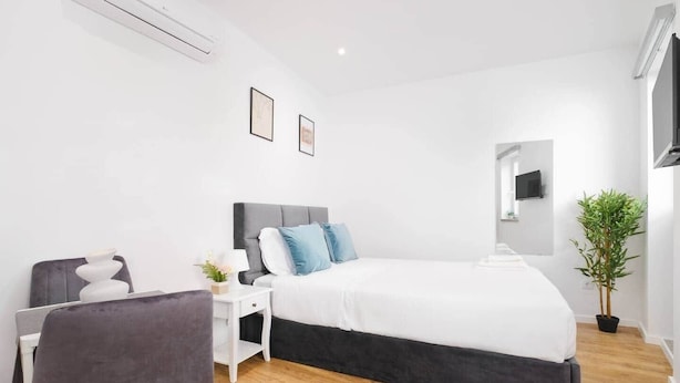 Een moderne slaapkamer met een bed, nachtkastje, stoel en een potplant.