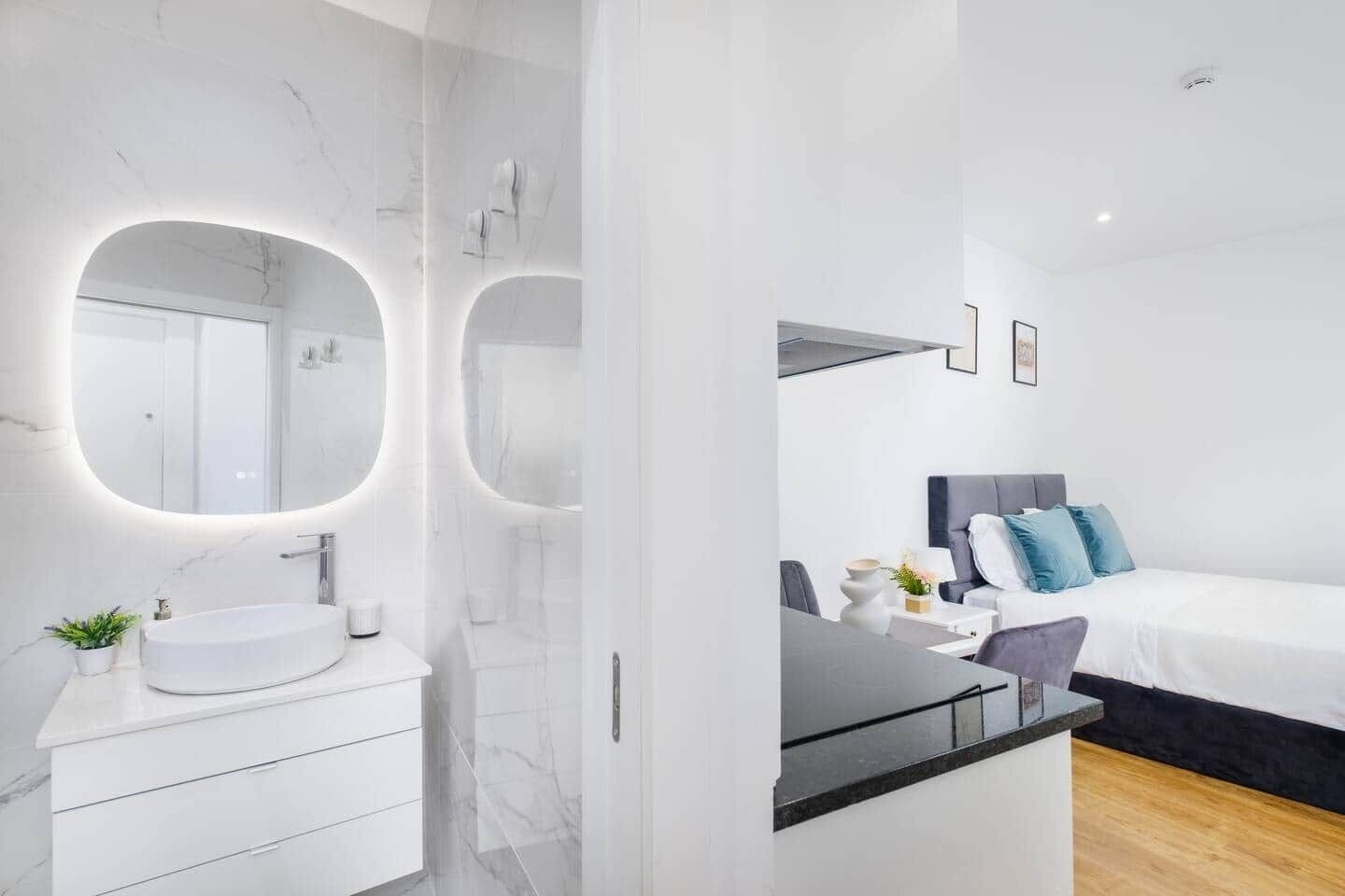 A modern hotel room with a marble bathroom, a large bed with blue pillows, and a small bedside table with a vase.