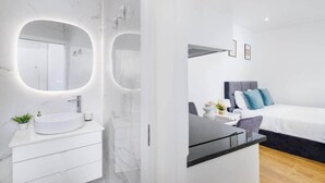 Een moderne hotelkamer met een marmeren badkamer, een groot bed met blauwe kussens en een klein nachtkastje met een vaas.