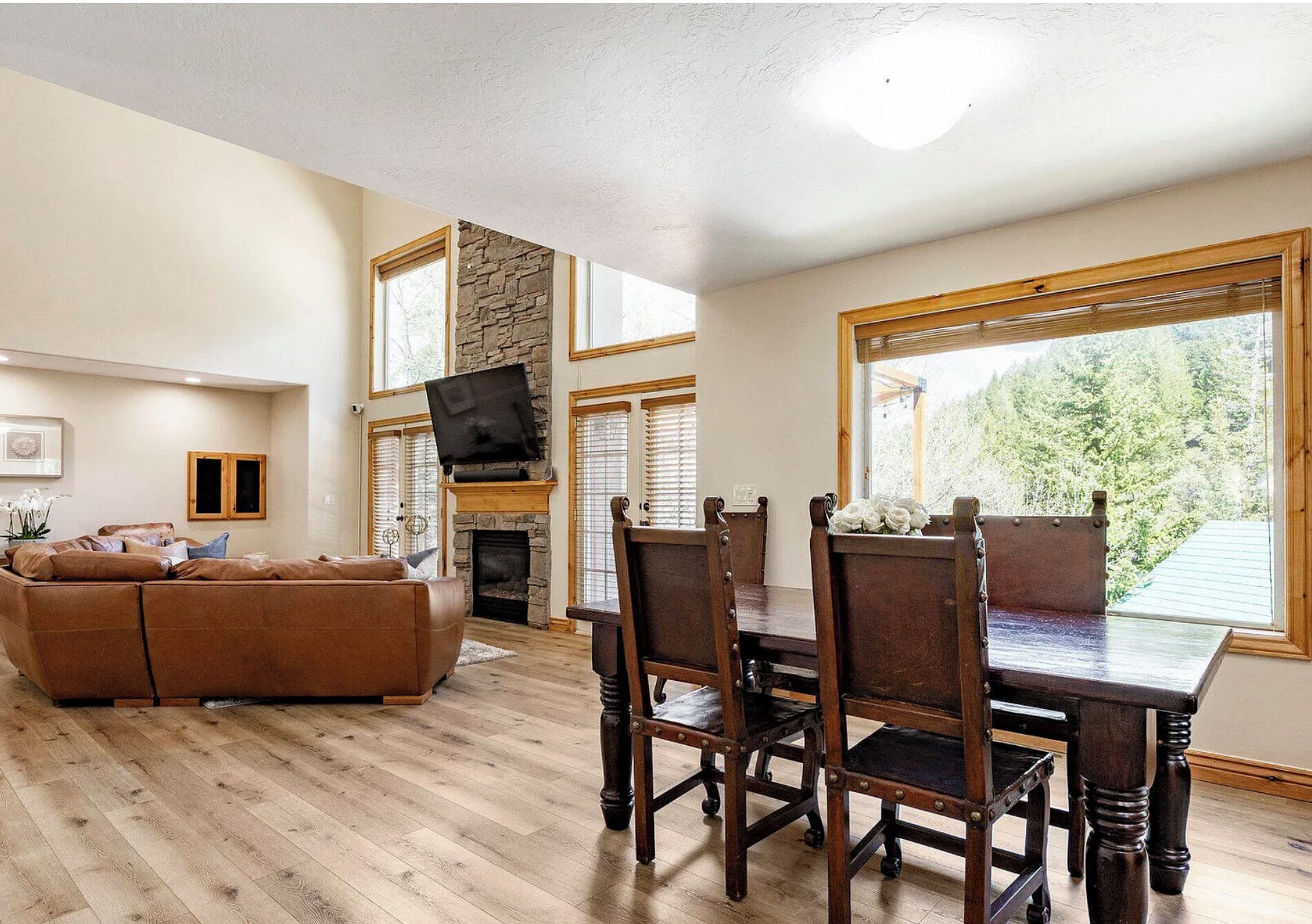 A living room with a stone fireplace, wooden dining table, and a brown leather sofa.