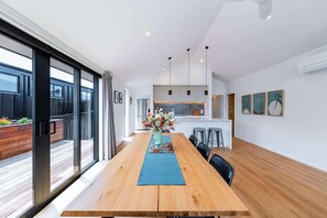 A spacious dining area with a wooden table, a blue runner, and a vase of flowers. - Mountainlight Escape - With Lake and Alpine Views (Wānaka)