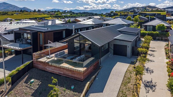 A modern residential area with contemporary houses featuring large windows, flat roofs, and a mix of open and enclosed spaces. - Mountainlight Escape - With Lake and Alpine Views (Wānaka)