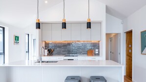 Une cuisine moderne avec un plan de travail blanc, deux tabourets de bar et des luminaires suspendus.