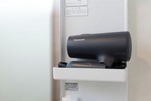 A Panasonic hair dryer mounted on a white wall with a label and a power outlet below it.