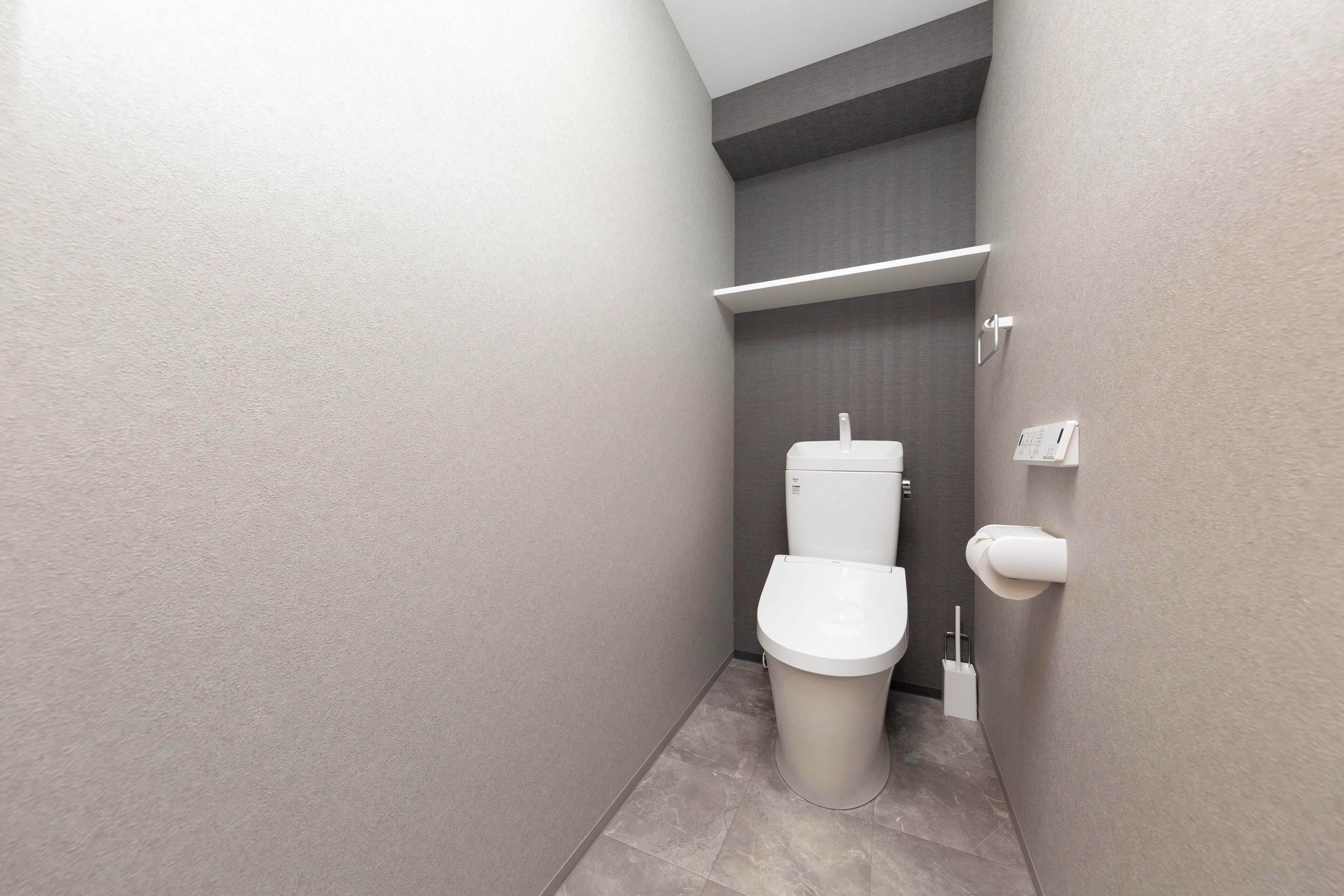 A compact, modern bathroom with a toilet, a small shelf, and a hand dryer.