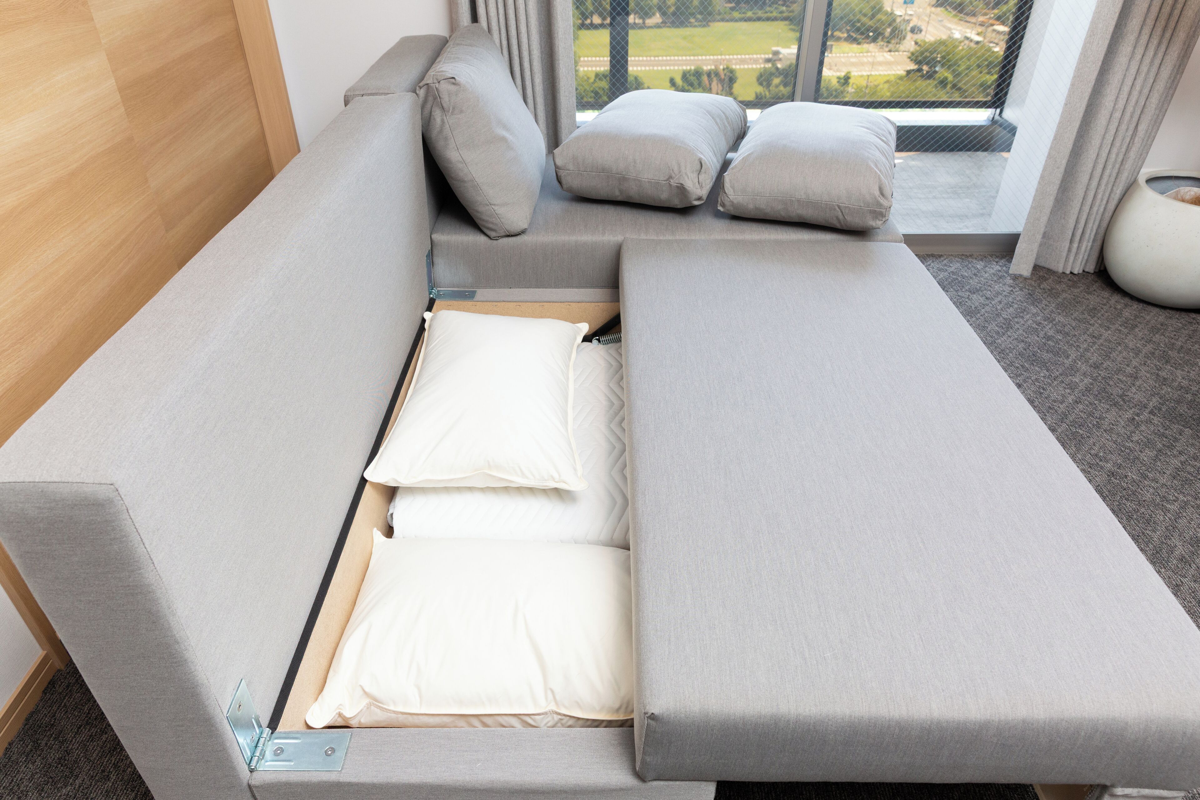 A modern room with a convertible sofa bed, a view of the outdoors, and a small potted plant.