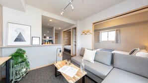 A modern living room with a sofa, a coffee table, a plant, and a bookshelf. - Residence Hotel Hakataekiminami (Fukuoka)