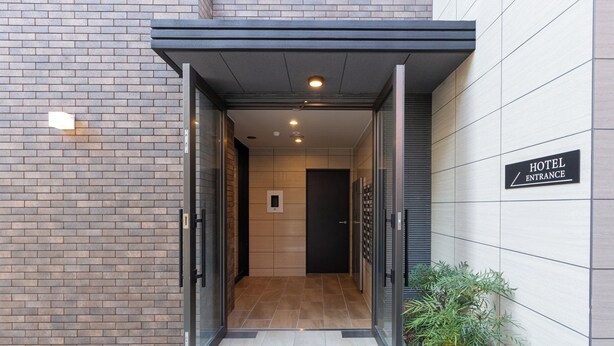 A hotel entrance with a modern design, featuring a brick facade, a glass door, and a sign indicating the entrance. - Residence Hotel Hakataekiminami (Fukuoka)