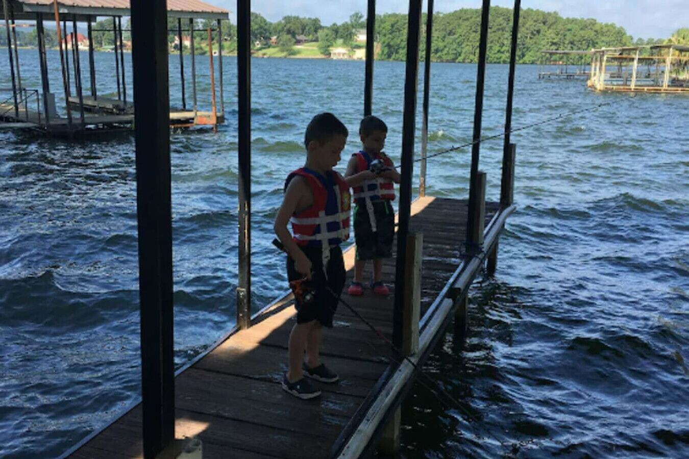 Zwei Personen auf einem hölzernen Steg, der ins Wasser führt, tragen Rettungswesten.