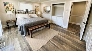 A bedroom with a bed, bedside tables, a ceiling fan, a walk-in closet, and a door leading to another room. - The Lake House at Sunset Bay (Hot Springs)