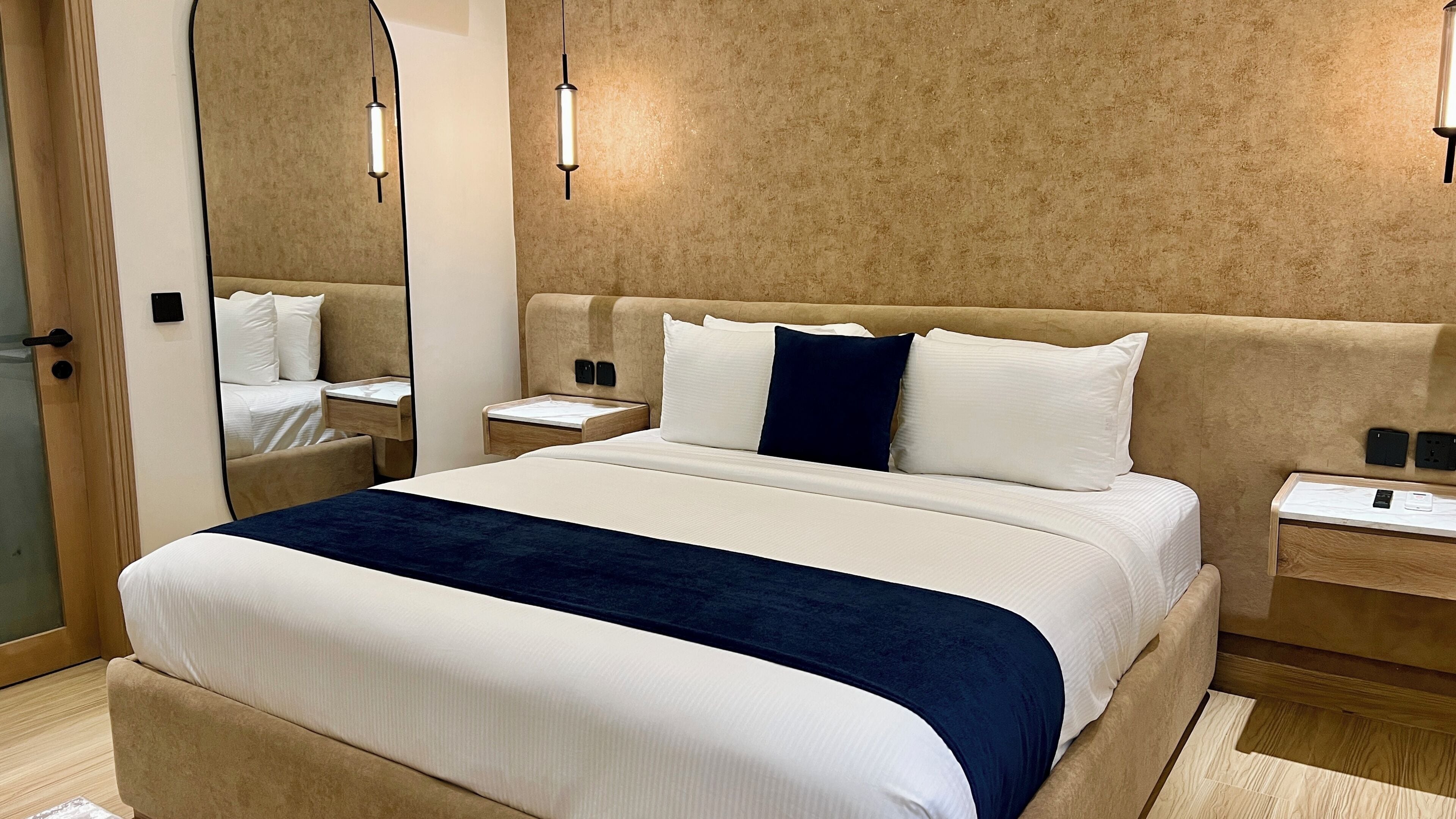 A hotel room with a large bed, bedside tables, a mirror, and wall-mounted lighting.