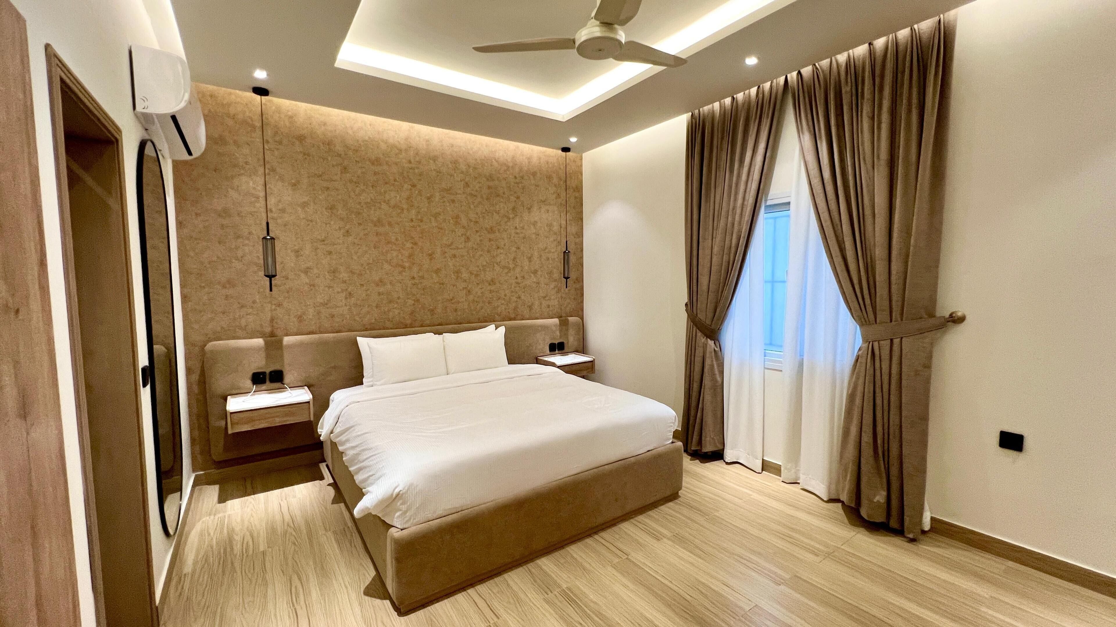 A modern bedroom with a large bed, a ceiling fan, a nightstand, and a window with curtains.