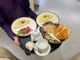 Una bandeja con dos platos de comida, una cesta de pan, un hervidor y una taza.