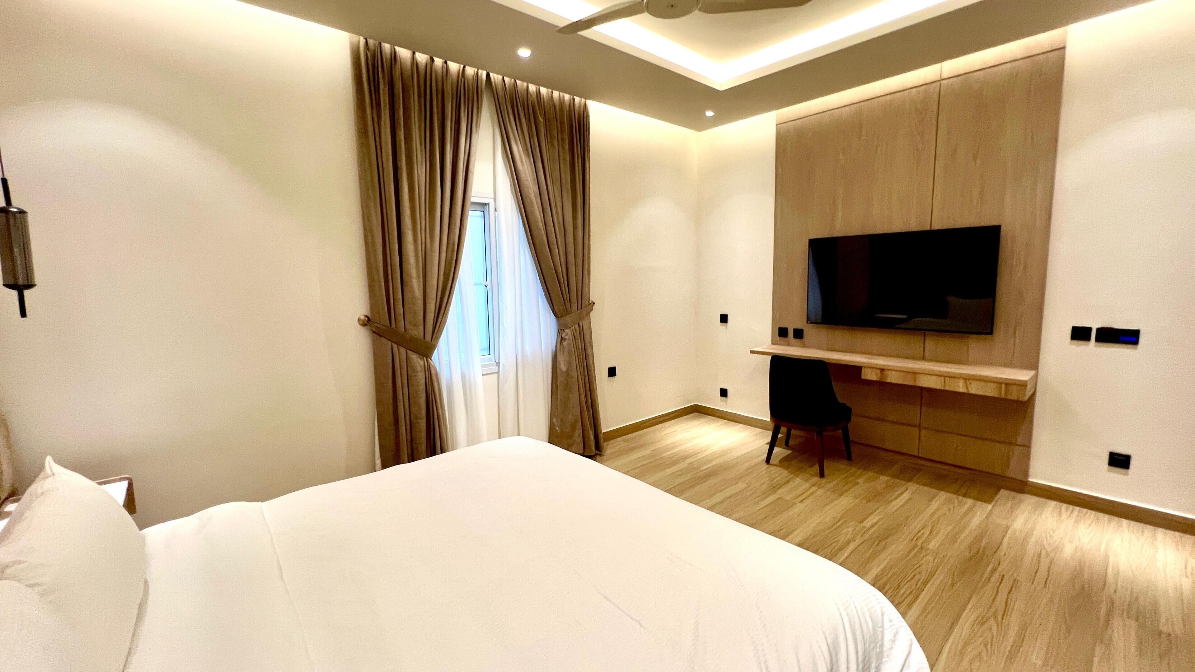 A modern hotel room with a large bed, a TV mounted on the wall, and a desk.
