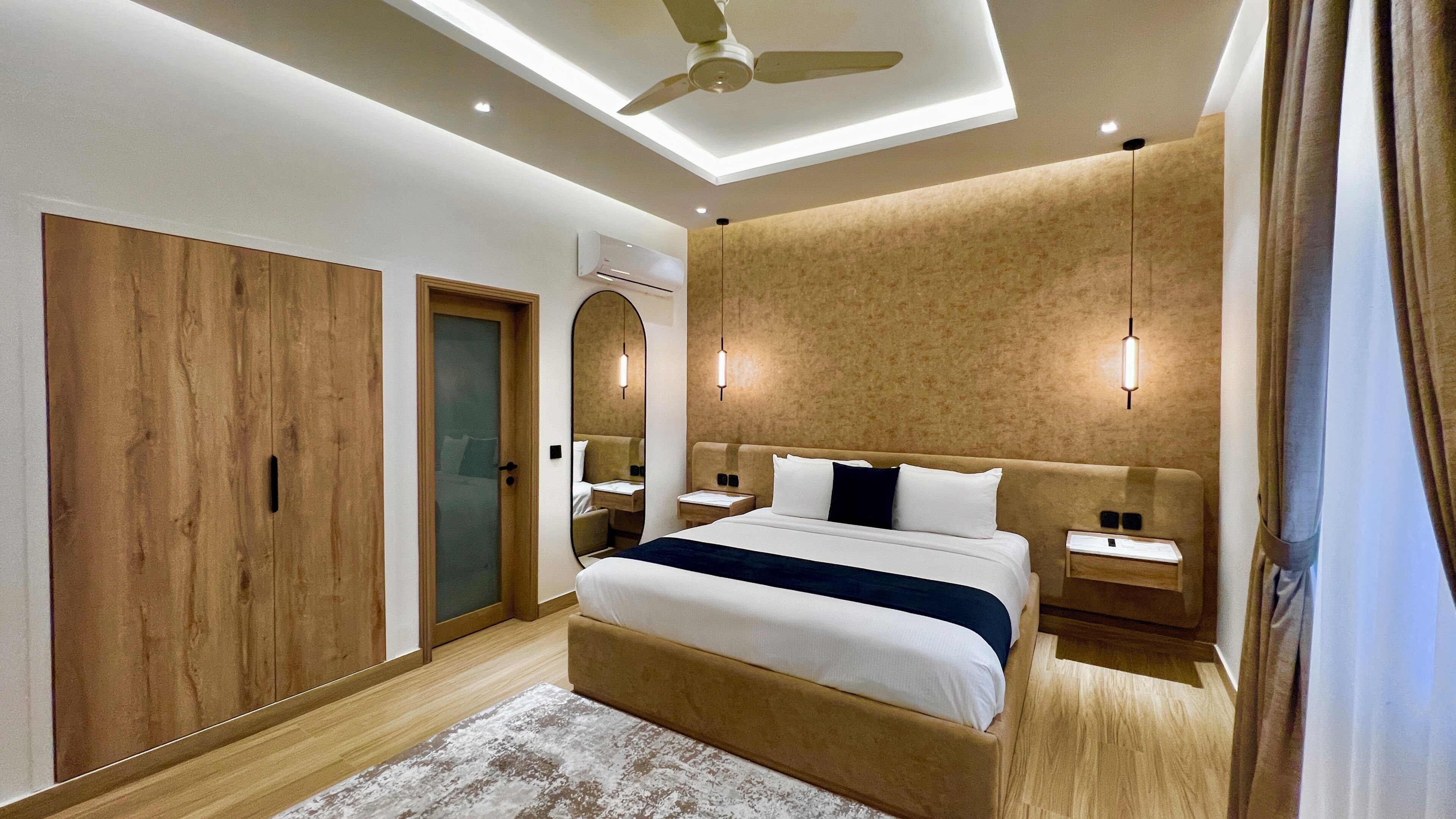Camera d'albergo moderna con un letto grande, un armadio in legno, una ventola a soffitto e luci a parete.