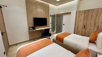 Habitación de hotel con dos camas, un escritorio con televisor, una silla y un armario.