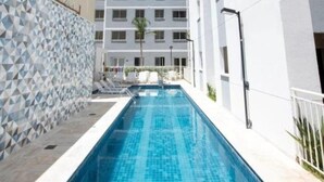 Ein Schwimmbecken mit einem geometrischen Fliesenmuster, umgeben von einem weißen Gebäude mit mehreren Fenstern und Balkonen.