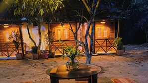 An outdoor wooden table with benches, surrounded by potted plants and trees, with a building in the background. - Dolubari Eco Resort Sreemangal (Kamalganj)