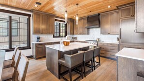 Une cuisine moderne avec un plafond en bois, de grandes fenêtres et un îlot central doté de tabourets de bar.