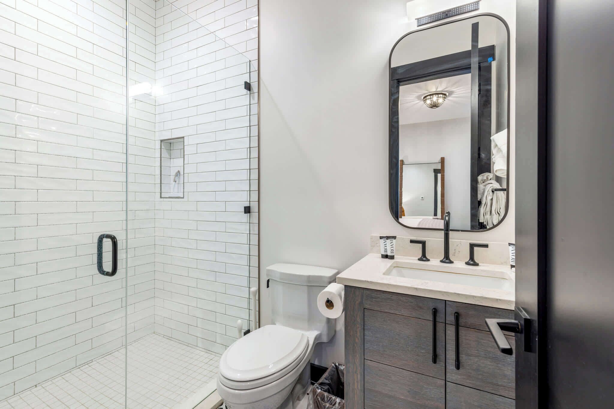 Een moderne badkamer met witte metro tegels, een douche met glazen wanden, een toilet en een wastafelmeubel met spiegel.