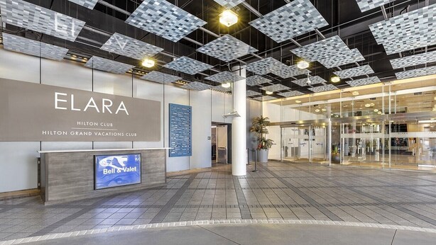 Un hall d'hôtel moderne, avec une grande enseigne ELARA, un service de bagagerie et de voiturier, et une entrée en verre.