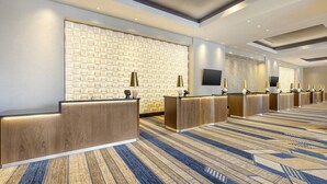 Un espace d’accueil d’hôtel comprenant plusieurs comptoirs de réception, un mur décoré de motifs et une moquette à motifs.