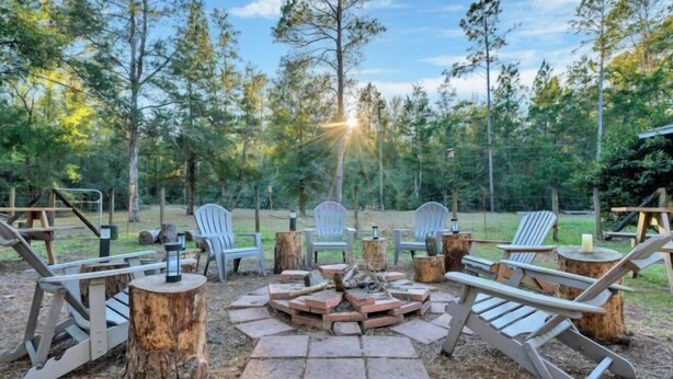 A fire pit surrounded by Adirondack chairs in a forested area. - Bnb Hyperion 4B2B Home w Firepit, Hot Tub & Pond (Eustis)