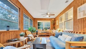 A cozy room with wooden walls, large windows, a ceiling fan, and a blue sofa. - Bnb Hyperion 4B2B Home w Firepit, Hot Tub & Pond (Eustis)