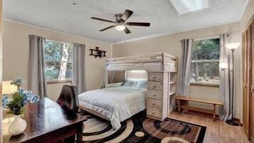 A bedroom with a bunk bed, a desk with a chair, a ceiling fan, and a window with curtains.