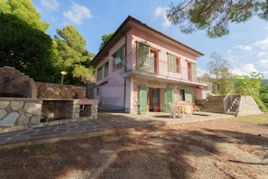 Ein zweistöckiges Haus mit einer Naturstein-Fassade, einem Balkon und einer Terrasse mit Gartenmöbeln.