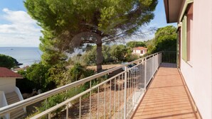 A balcony with a metal railing overlooking a coastal area with trees and a view of the sea.