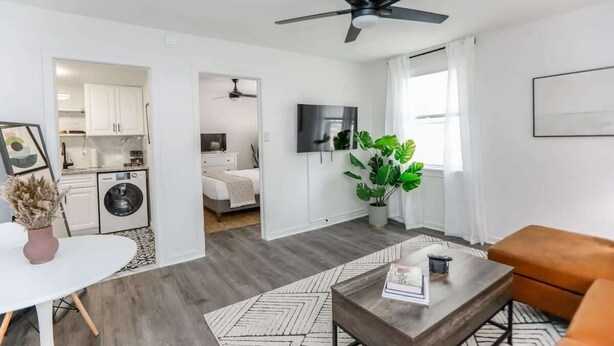 A modern apartment with a living room, kitchen, and bedroom. It features a ceiling fan, a flat-screen TV, and a potted plant. - Sojourn | The South Shore Apartments (Norfolk)