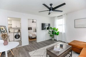 Een modern appartement met een woonkamer, keuken en slaapkamer. Het heeft een plafondventilator, een flatscreen-tv en een kamerplant.